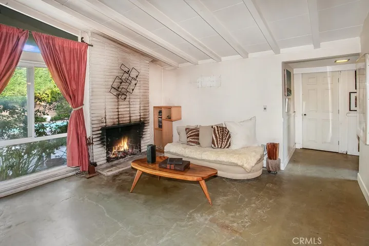 The family room is bathed in natural light from a multitude of windows and is enhanced by pitched wood beamed ceilings, track lighting, floor-to-ceiling brick fireplace, sliding glass doors that lead to the backyard and concrete floors.