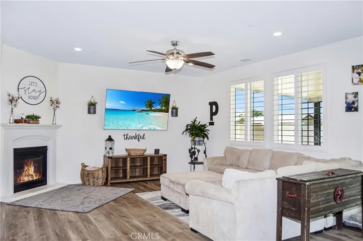 The living room area offers a cozy gas fireplace, waterproof luxury vinyl plank flooring, a ceiling fan, recessed lighting and lots of windows looking out on the backyard