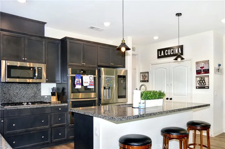 The gorgeous kitchen features dramatic dark cabinetry with plenty of storage including pot and pan drawers, quartz countertops, stainless steel appliances, a farmhouse-style sink, a breakfast bar, a double-door pantry, and pendant lighting