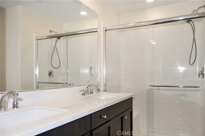 Main suite bath with dual sinks atop dramatic dark cabinetry, a walk-in shower with glass enclosure, and a private water closet.