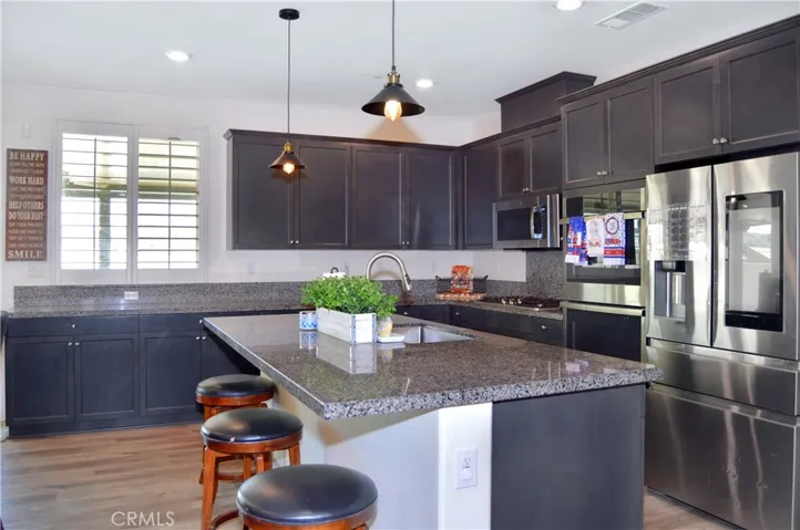 The gorgeous kitchen features dramatic dark cabinetry with plenty of storage including pot and pan drawers, quartz countertops, stainless steel appliances, a farmhouse-style sink, a breakfast bar, a double-door pantry, and pendant lighting