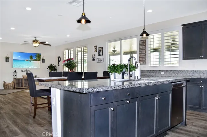 The gorgeous kitchen features dramatic dark cabinetry with plenty of storage including pot and pan drawers, quartz countertops, stainless steel appliances, a farmhouse-style sink, a breakfast bar, a double-door pantry, and pendant lighting
