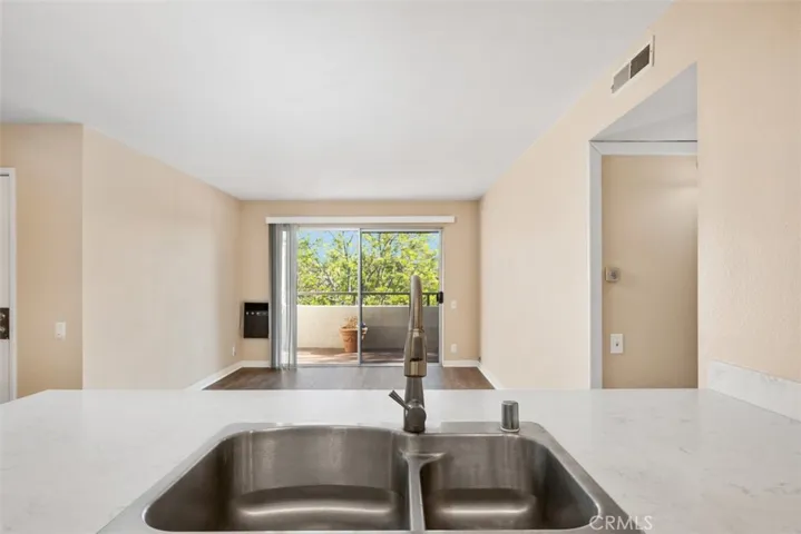 View from behind the kitchen sink towards the living room out of the sliding door to the balcony to the view of the trees.