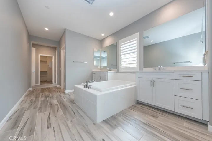 standing with back to built-in linen storage cabinet, note two individual sink & countertop areas, separated by big bathtub, looking out towards primary bdrm closet, just inside the primary suite