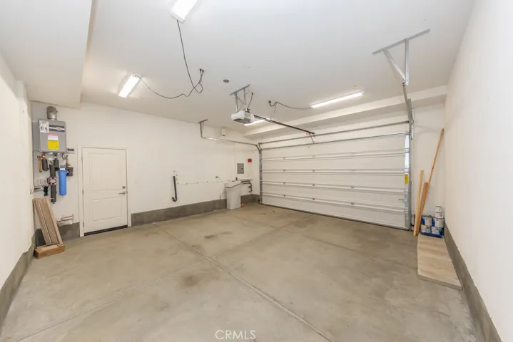 Spacious FINISHED garage, picture taken from standing in garage access door near entry; note water softener on right (included!) and tankless water heater (with recirculator!) at left, next to side yard door.  Spare flooring & spare paint shown can be included upon request at no charge, just add them into your offer