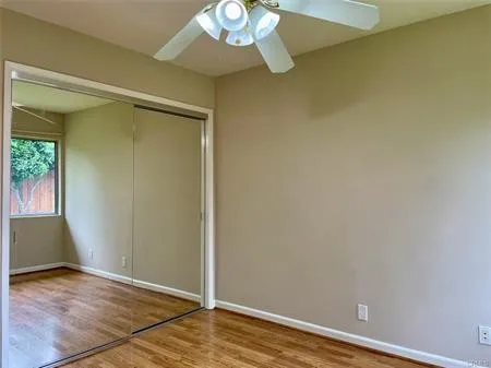 One of the second bedrooms with the ceiling fan, mirrored wardrobes and window looking outside.