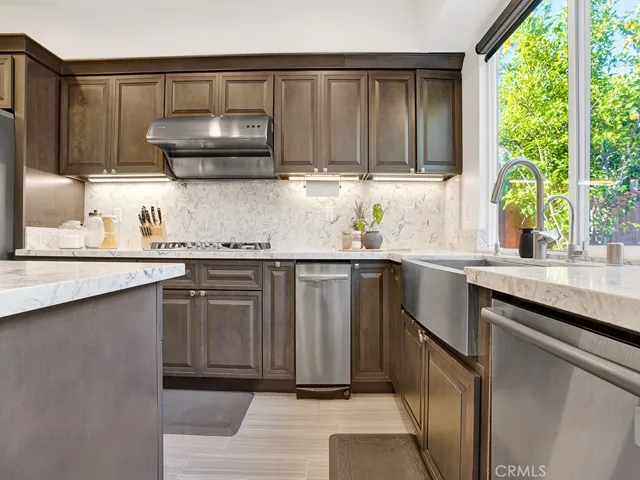 View of the cooktop, trash compactor, stainless farmhouse sink, stainless dishwasher