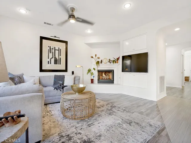 Large family room that overlooks the kitchen and breakfast dining table complete with gas fireplace, freshly painted, wood blinds, a beautiful view of the backyard, built-in TV cabinet, and modern ceiling fan.