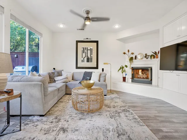 Large family room that overlooks the kitchen and breakfast dining table complete with gas fireplace, freshly painted, wood blinds, a beautiful view of the backyard, built-in TV cabinet, and modern ceiling fan.