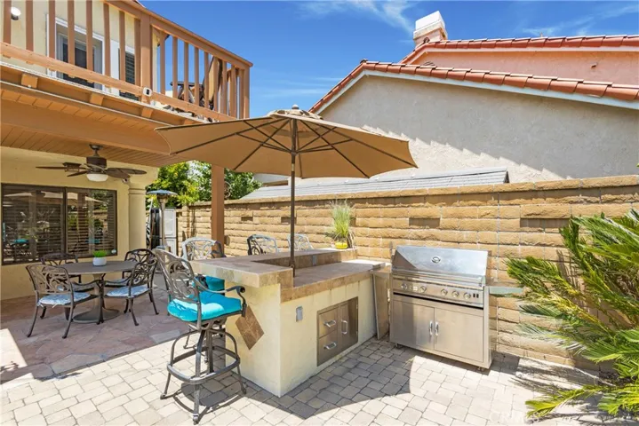 Built in bar with barstool seating, a barbeque, and a covered patio with a ceiling fan