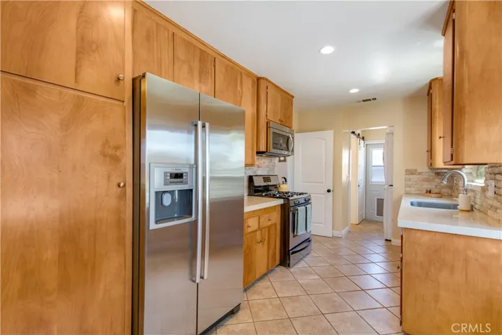 Beautiful, cute kitchen including well-kept tile floors, warm wooden kitchen cabinets with self-closing drawers and stainless-steel refrigerator.