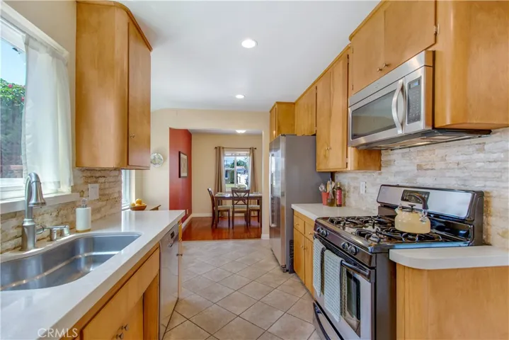 View from laundry room onto cute kitchen and dining area and 4 burner gas stove and oven and above stove stainless-steel microwave.