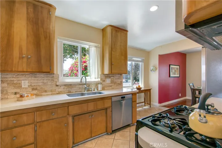 View of cute kitchen view of warm wooden cabinets with self-closing drawers and stainless-steel dishwasher and sink.