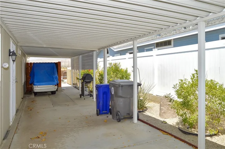 Carport/driveway/back door side of the home with protected golf cart parking area, tall vinyl fencing, and greenery along the side
