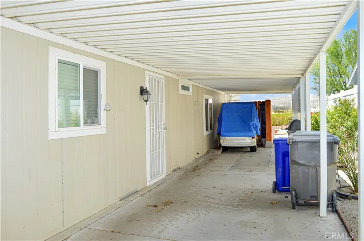 Carport/driveway/back door side of the home with protected golf cart parking area, tall vinyl fencing, and greenery along the side