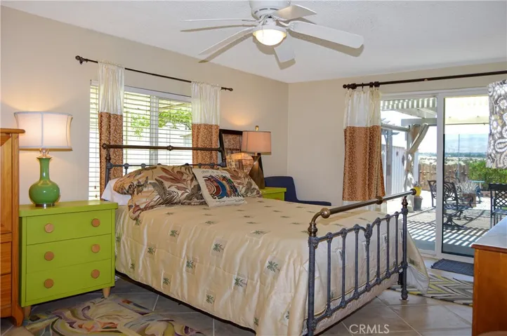 The main bedroom suite sits at the back of the home with a sliding door offering backyard access and desert views, a ceiling fan, tile flooring, and an en suite bath
