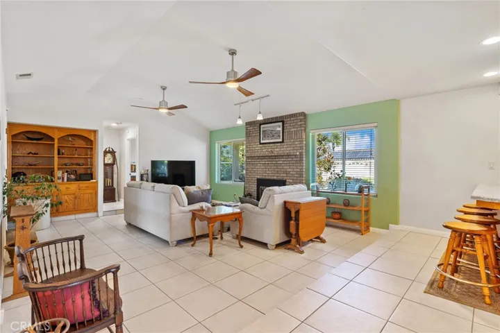 Family Room: tile flooring, brick fireplace mantle & raised hearth with zero clearance gas fireplace with remote, custom ceiling fan/lights, hanging accent lamps, custom built-in bookshelves & cabinets, vaulted ceiling, kitchen breakfast bar at right, doorway to Office/4th bedroom & hallway to laundry room & 3rd bathroom & garage at rear.