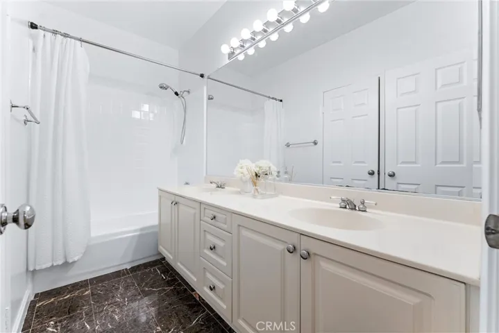 Hallway bathroom with tub in shower and dual vanity.