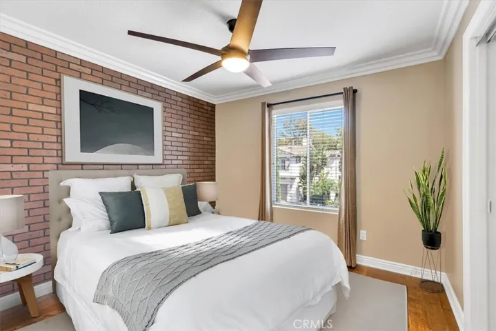 **VIRTUALLY STAGED** Bedroom 3 features a brick veneer accent wall, crown molding, mirrored closet doors, designer ceiling fan, and window overlooking the front yard.