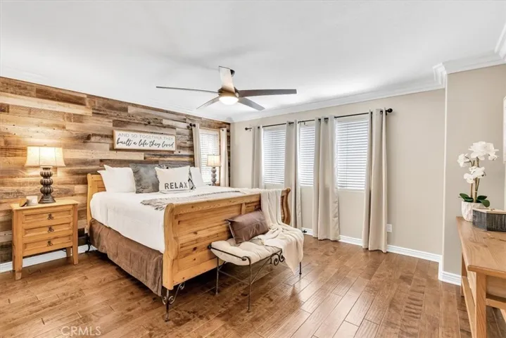 With a custom wood barn accent wall, the spacious primary bedroom is filled with natural light. The hardwood floors continue upstairs, as do the upgraded baseboards and crown molding, and a designer ceiling fan tops it off.