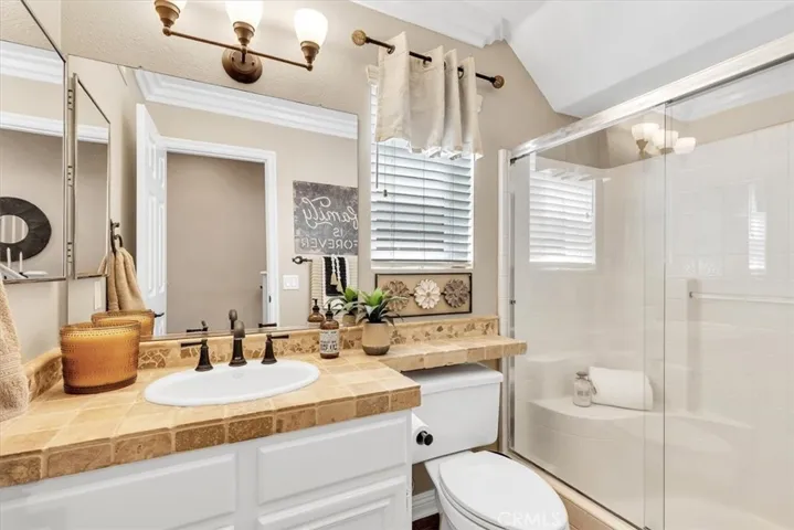 Adjacent to the main floor bedroom, the guest bath features a step-in shower with glass enclosure, tumbled stone countertop, Kohler sink, designer light fixture, freshly painted cabinetry with modern black hardware.