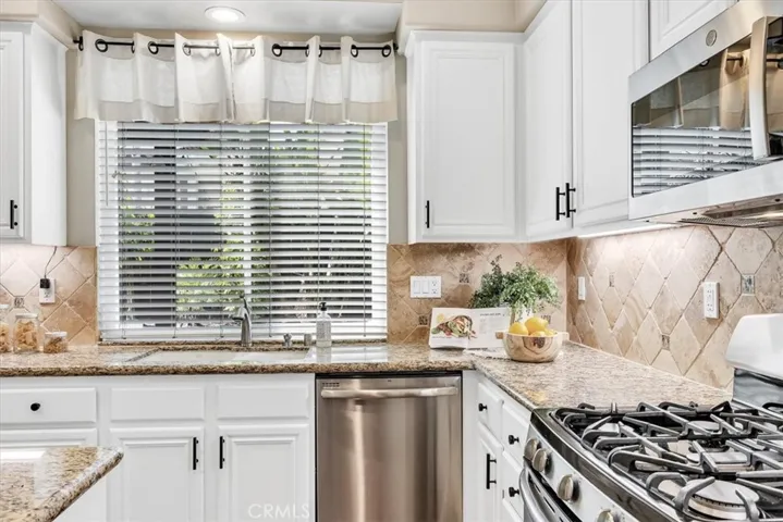 Equipped with granite counters, fresh white cabinets with modern black pulls & hardware, and stainless steel appliances, including a new microwave. The window over the sink looks out to the back patio & garden.