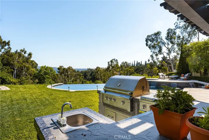 The kitchen features a large gas BBQ, two additional gas burners, large prep area, bar, refrigerator and sink.