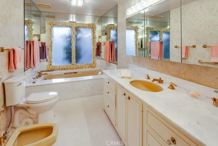 Separate privacy room with marble crowned vanity, undermount basin, large dressing mirror with sundry/medicine storage, custom Hollywood style lighting, soaking tub with marble surround, commode and bidet.