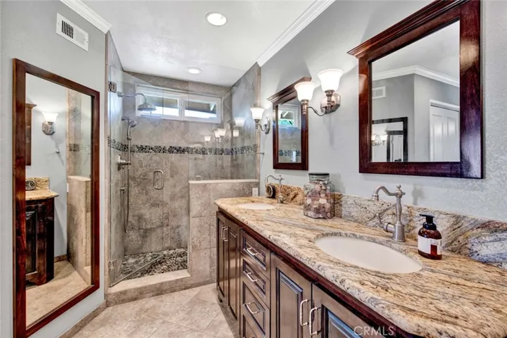 Primary Suite Luxurious Bathroom with Granite Counters, Dual Sinks, Oversized Walk-In Shower with Sitting Bench and Hidden Shampoo Niche, Designer Tile Walls with Pebble Inlay
