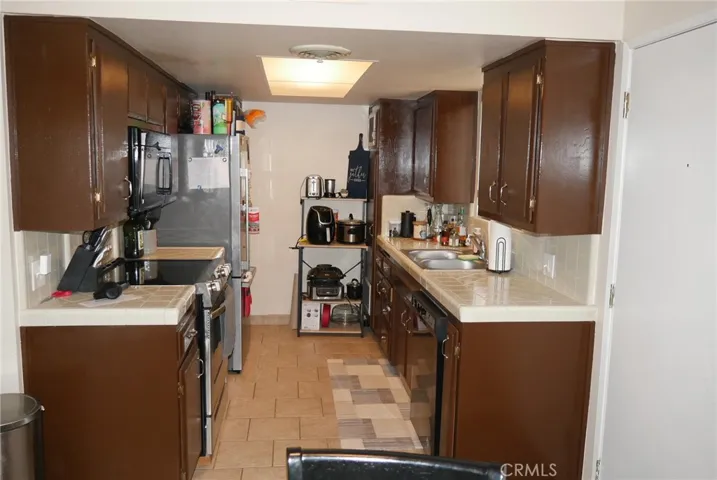 Kitchen: tile flooring, tile countertops & full backsplashes, dishwasher, disposal, electric range, microwave oven, vent hood, stainless steel double sink, lots of cabinets.
