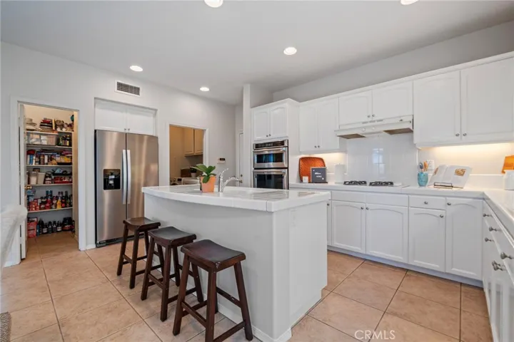 Designed for functionality and style, the kitchen features white cabinets, stainless steel appliances, a spacious island,  walk-in pantry, and is open to the family room.