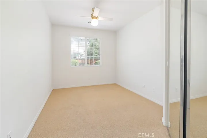 Bedroom 1 offers a mirrored closet door, a ceiling fan with light and carpet flooring.