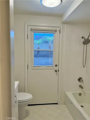 An additional view of the hall bathroom/laundry room with a shower combination storage and door that leads to the backyard.