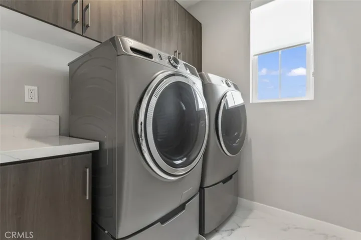 LAUNDRY ROOM WITH BUILT-IN UPPER CABINETRY. FRONT LOAD WASHER/ DRYER WITH LAUNDRY PEDESTALS.