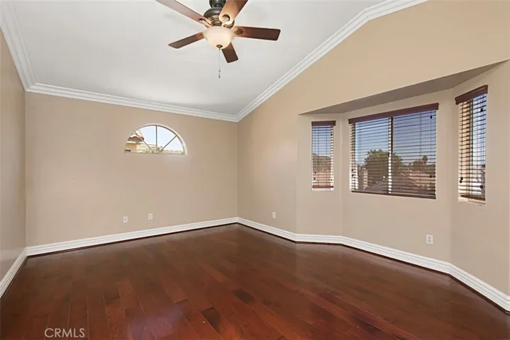 Primary bedroom has rich wood floors, wooden blinds & ceiling fanlight