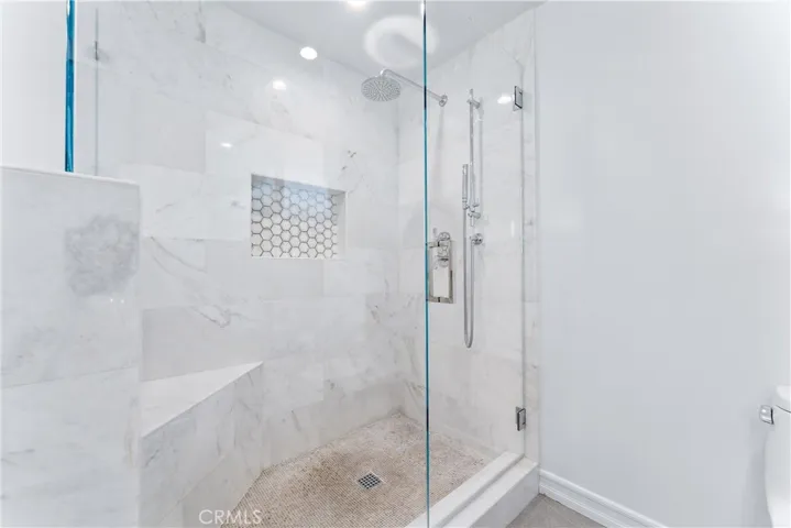Marble shower with honeycomb tile inset toiletry shelf, rain shower head, full height ceiling shower door for warmth and a corner bench.