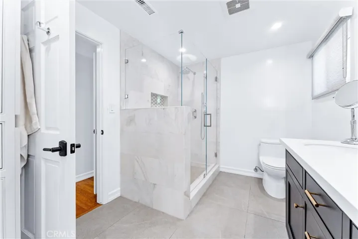 Wide tile marble floor blends with the marble of shower and contrasts with the beautiful dark wood vanity.