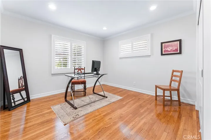 Home office with gleaming hardwood floors, custom plantation shutters and closet highlight modern style and thoughtful functionality with outlets located in center of wall (for TV) and in floor for seamless plug in capability.