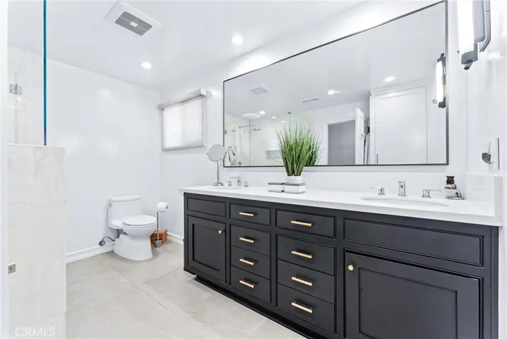 Primary bath with dual vanity and oversized mirror with diamond like accent lighting. Rain shower (feels like being under a waterfall) Marble shower details incl: corner bench, honeycomb tile shelf, and specialized tile shower flooring make each step a delight. Dark wood cabinetry featuring rich gold finishes make this bathroom retreat a star.