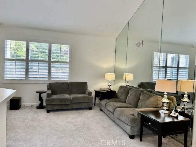 Large living room with Plantation shutters, high ceilng and fireplace with decorative logs. Living room is vacant and furniture removed.