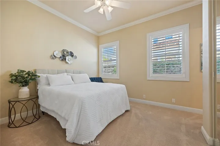 downstairs bedroom with ensuite bathroom, featuring a standing shower. Notice crown molding, mirrored closet doors, ceiling fan, and plantation shutters.