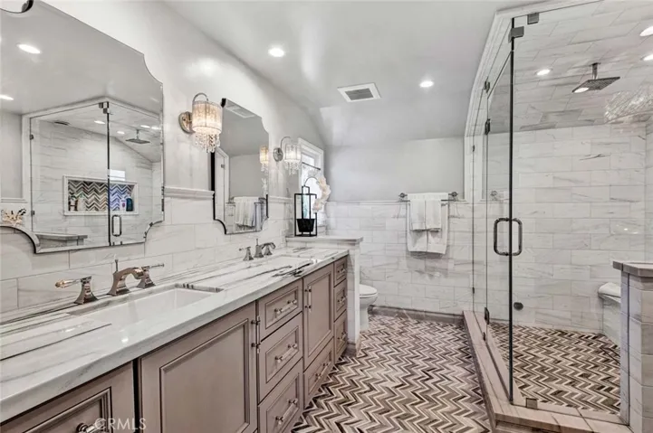 Primary Bathroom with Dual Sinks, 2 Vanities - One is Sit-Down Vanity, Sconce Lighting, Marble Wainscoting, Granite Countertops, and an Amazing Walk-In Shower with Marble Walls, Sitting Bench, Multiple Shower Heads, Floor-to-Ceiling- Clear Glass Enclosure, and is Plumbed to be a Steam Shower