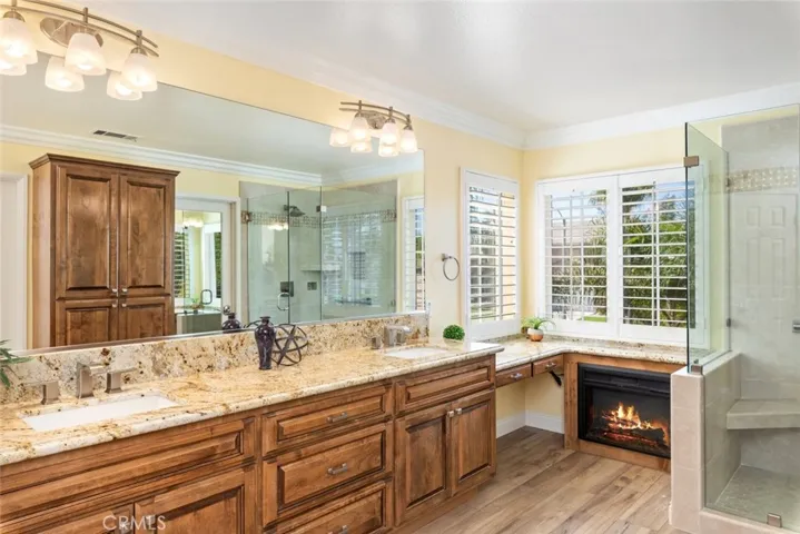 The luxurious primary bathroom has a spacious layout, granite countertops, a glass-enclosed shower, and a cozy fireplace.