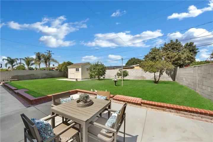 The expansive backyard is perfect for entertaining, featuring a shed/space with its own A/C unit, a raised grassy area with brick accents, fruit trees, and a block wall surround.