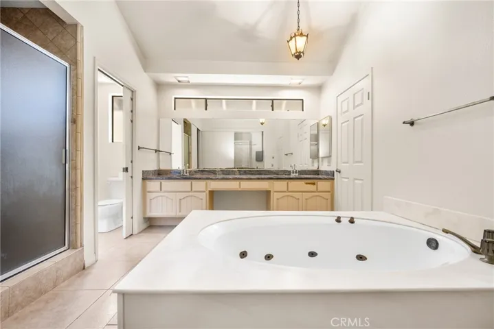 Primary Bathroom with Tile Flooring, Dual Vanities,  Spa Tub, and Granite Counters