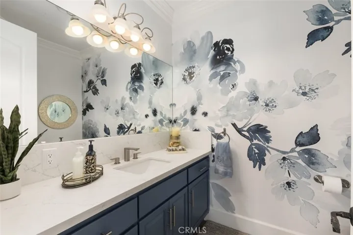 Entry guest bathroom features elegant floral wallpaper design & ample quartz counter vanity space.