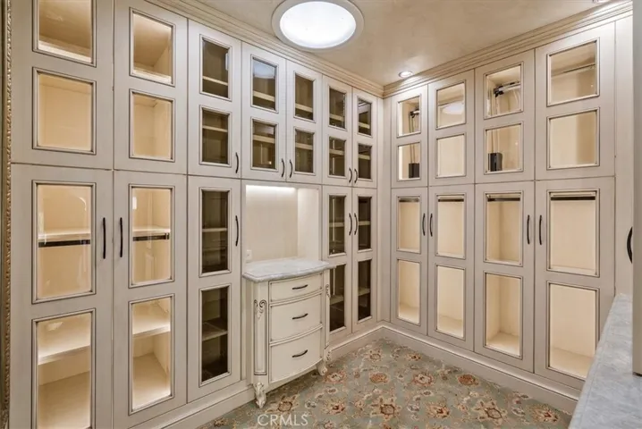 Walk-in closet featuring lighted glass cabinets and an automated pole system