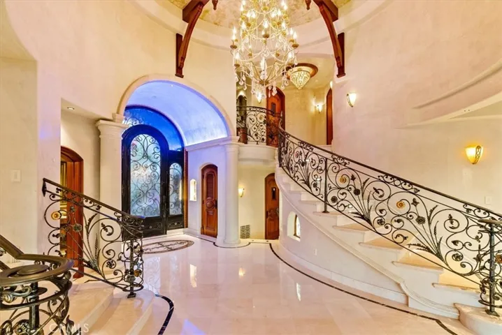 The chandelier, carved iron spiral staircase, and lighting add to the grandeur of the entry.