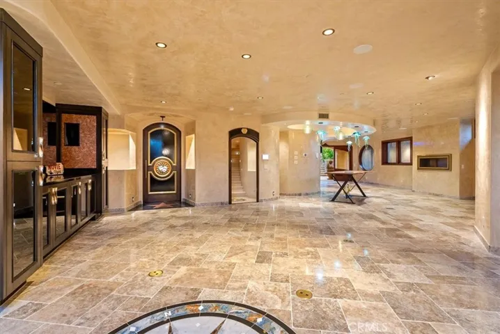 Expansive space tiled with travertine and plumbing in place for a built-in bar, with double door access to the outdoor courtyard