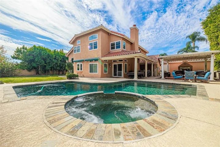 View from the spa and pool back toward the home. To the right is the outdoor living space with large covered, raised deck and patio, complete with a fireplace